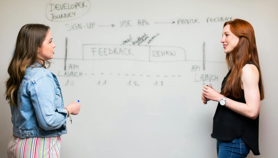 photo of women talking beside whiteboard